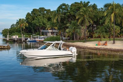 Chaparral 310 OSX anchored near the shore while a couple sits on the beach. 